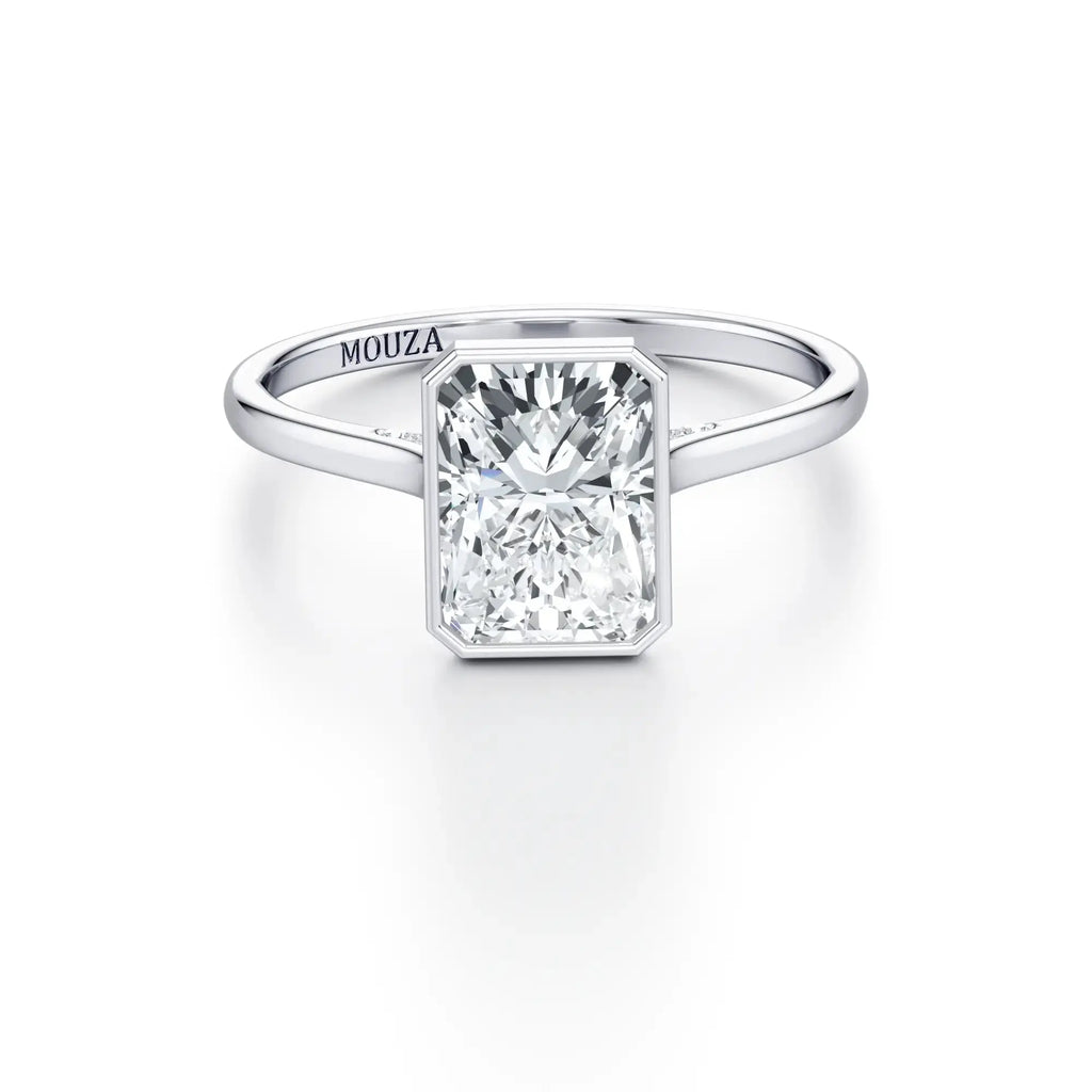 A white gold bezel set engagement ring with a clear central stone and micro-set stones on the bridge, labeled 'MOUZA' on the band.