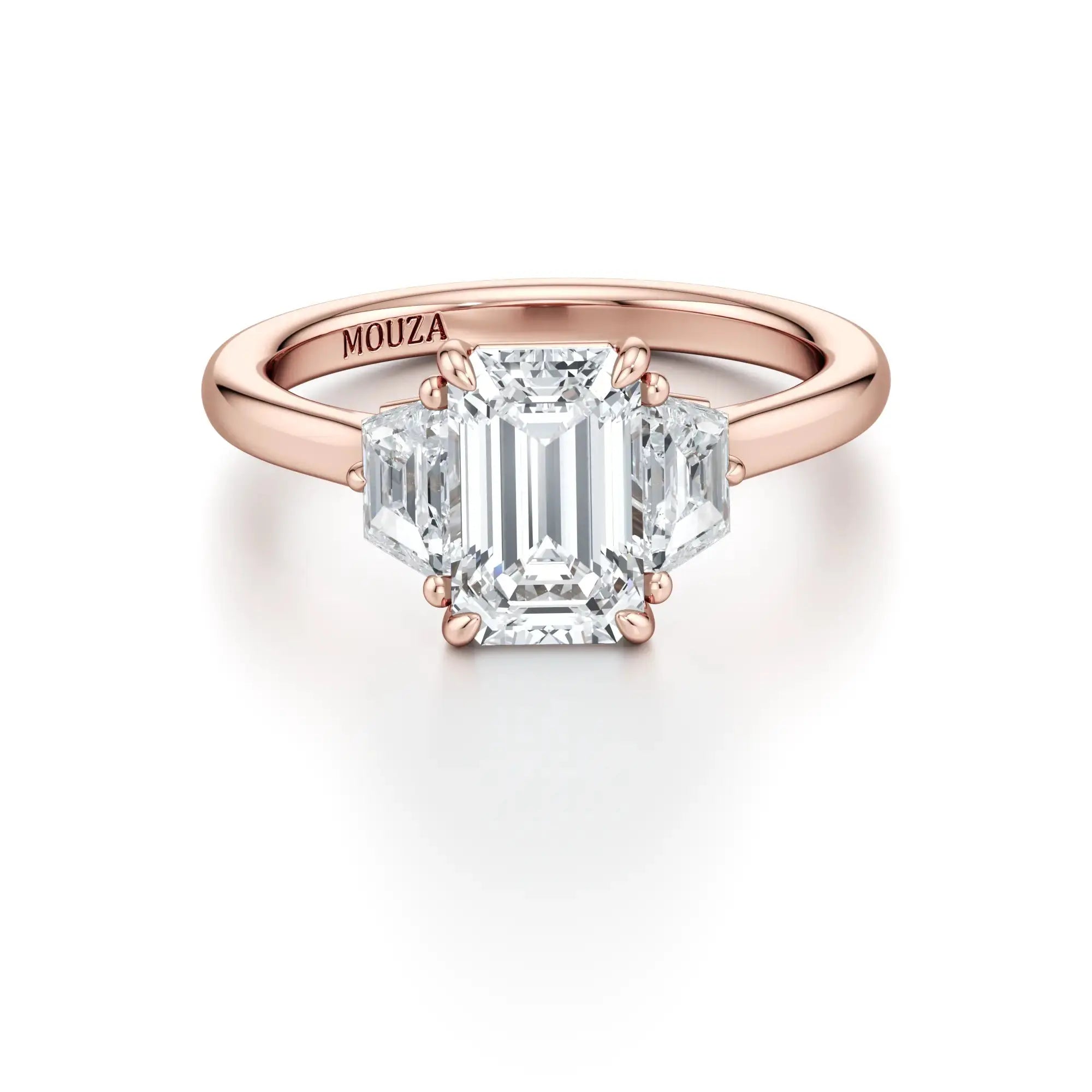 A sleek engagement ring featuring a central emerald-cut diamond flanked by two trapezoid-cut side stones, set in a rose gold band with the brand name 'Mouza' visible on the side.