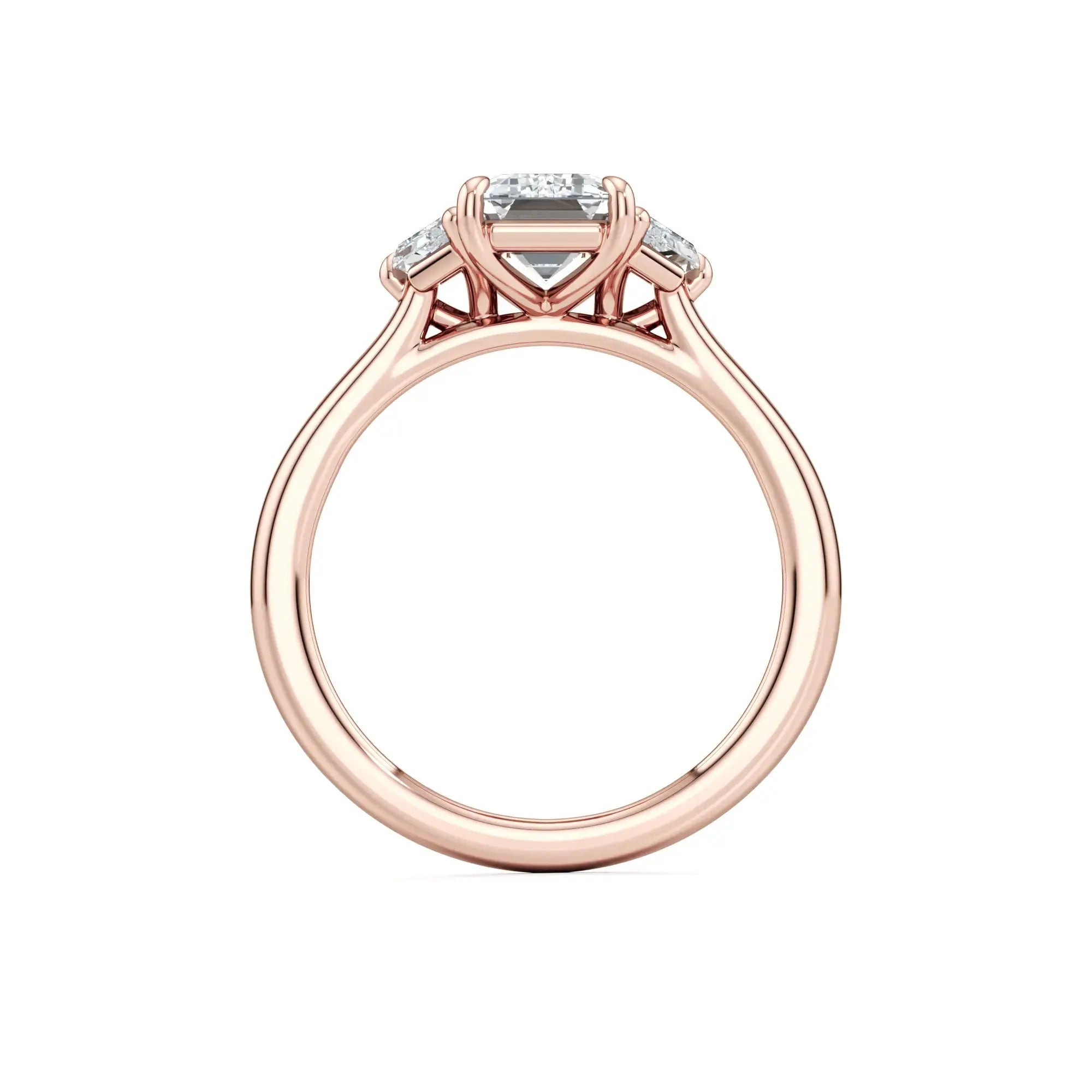 A sleek trilogy engagement ring featuring a central emerald-cut diamond flanked by two trapezoid-cut side stones, set in a rose band with the brand name 'Mouza' visible on the side.