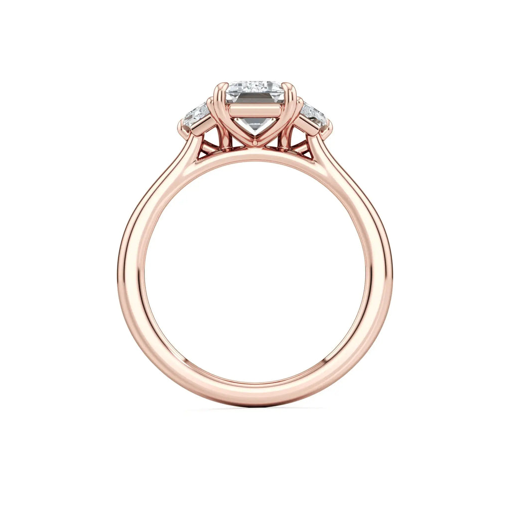 A sleek trilogy engagement ring featuring a central emerald-cut diamond flanked by two trapezoid-cut side stones, set in a rose band with the brand name 'Mouza' visible on the side.