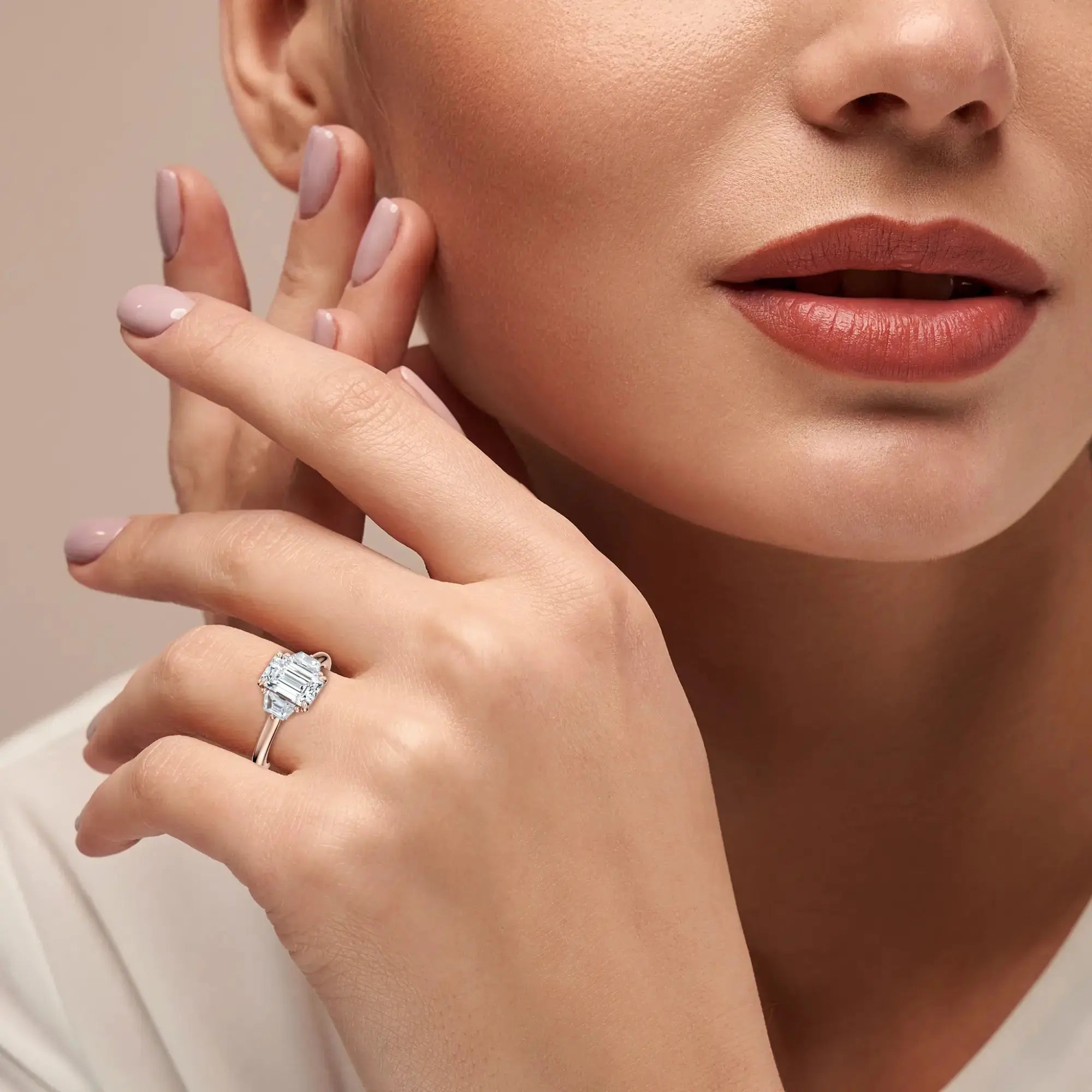 A sleek engagement ring featuring a central emerald-cut diamond flanked by two trapezoid-cut side stones, set in a rose band.