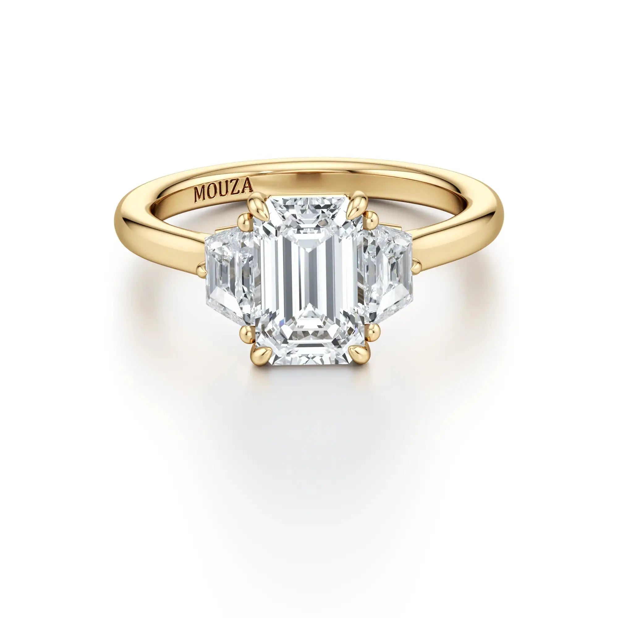 A sleek engagement ring featuring a central emerald-cut diamond flanked by two trapezoid-cut side stones, set in a gold band with the brand name 'Mouza' visible on the side.