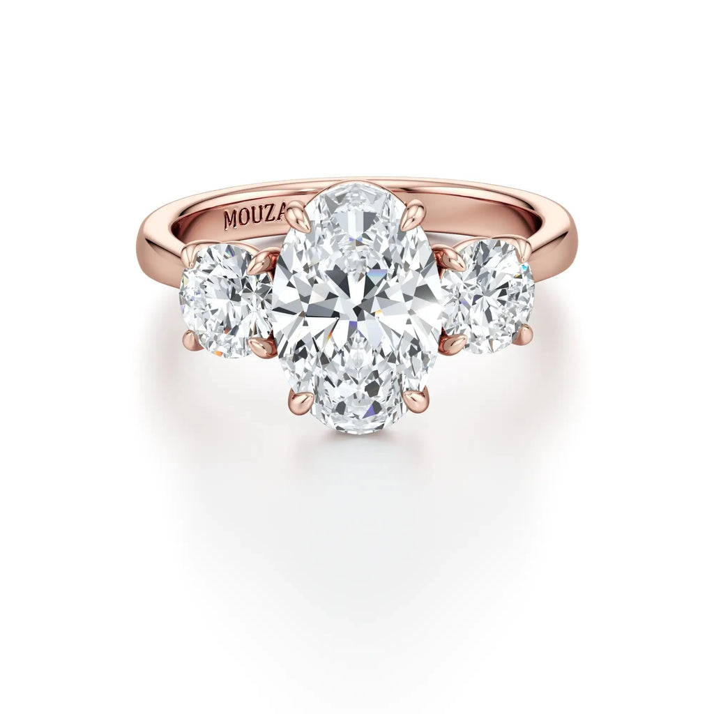 Rola - A classic three-stone engagement ring with round side stones and a central oval diamond, with 18K rose band having the brand name 'Mouza' on it.