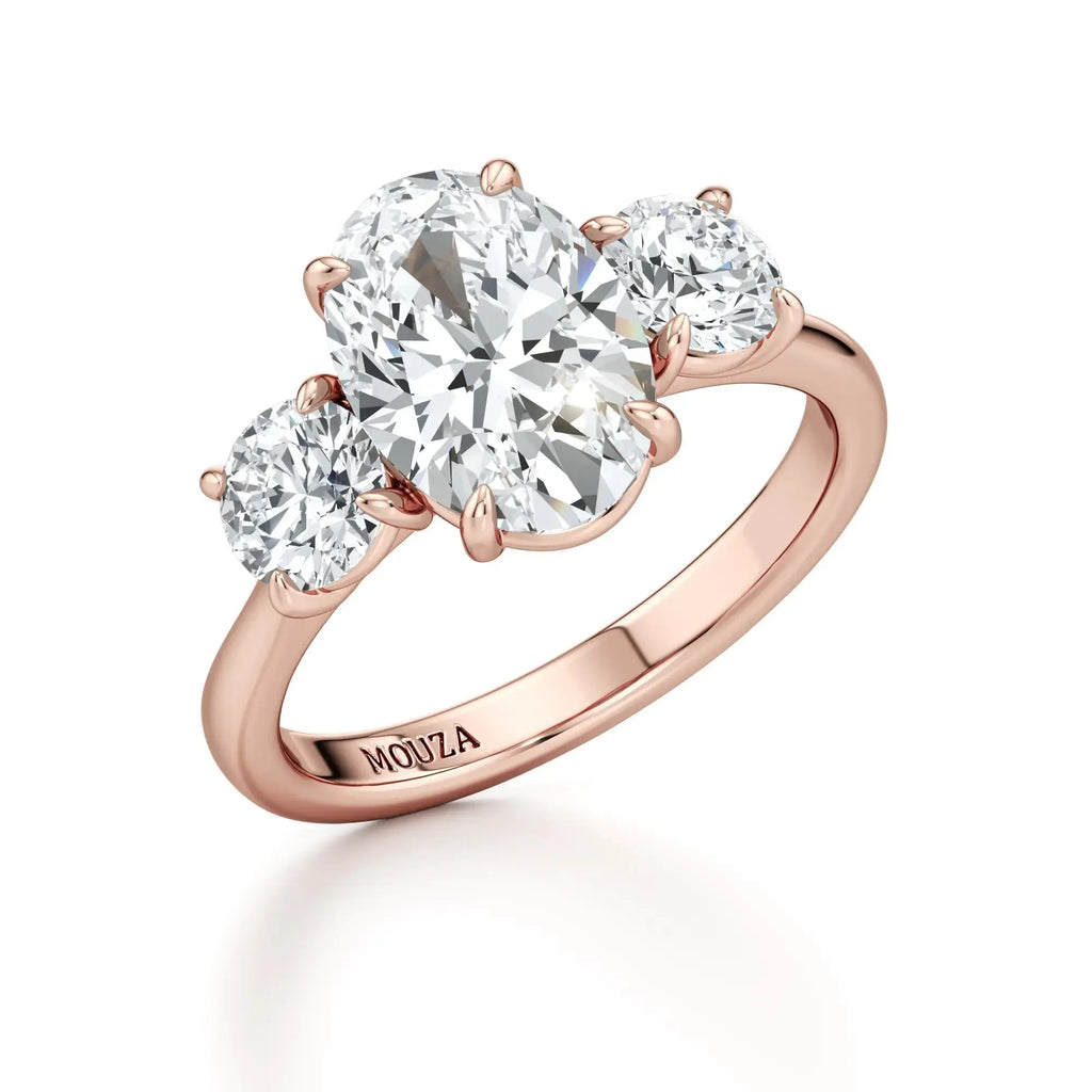 A classic trilogy engagement ring with round side stones and a central oval diamond, with rose band having the brand name 'Mouza' on it.