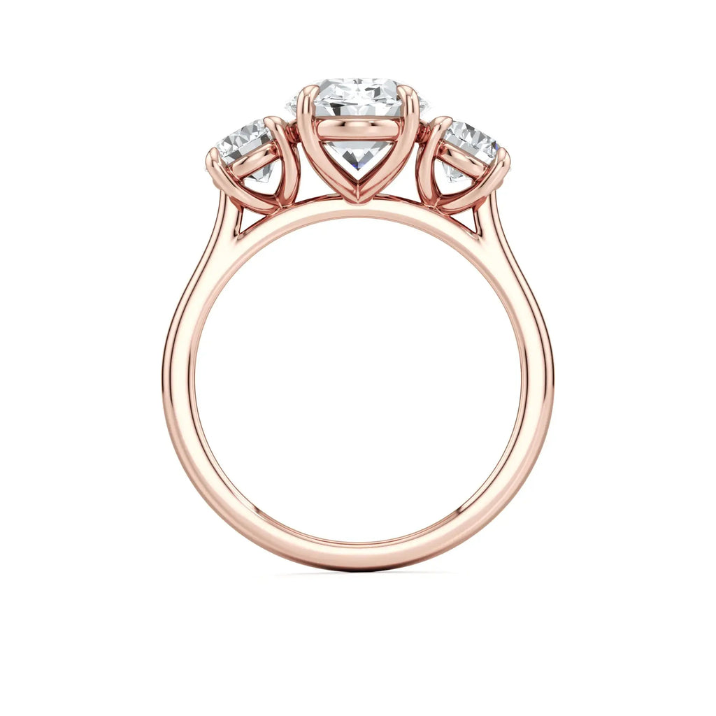 A classic three-stone engagement ring with round side stones and a central oval diamond, with a rose gold band having the brand name 'Mouza' on it.