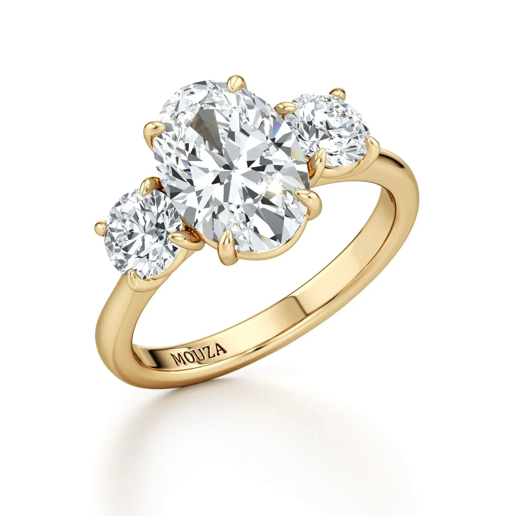 A classic trilogy engagement ring with round side stones and a central oval diamond, with 18k gold band having the brand name 'Mouza' on it.