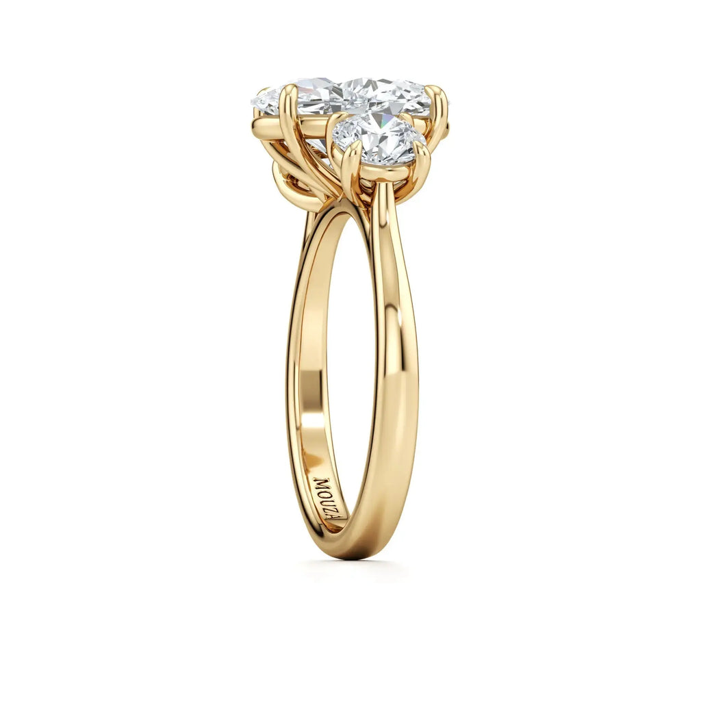 A classic three-stone engagement ring with round side stones and a central oval diamond, with 18K gold band having the brand name 'Mouza' on it.